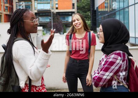 Tre buoni amici di diverse etnie che chiacchierano nel loro campus universitario Foto Stock