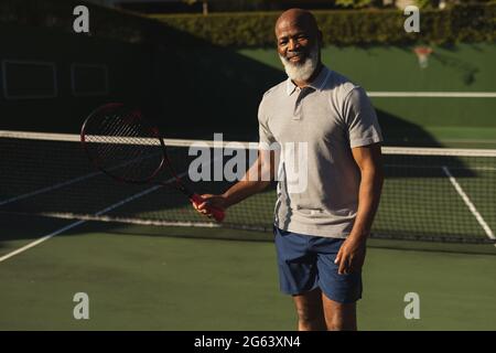 Sorridente uomo afro-americano che gioca a tennis sul campo da tennis Foto Stock