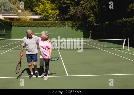 Coppia caucasica senior abbracciando e sorridendo sul campo da tennis Foto Stock