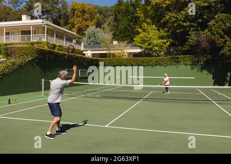 Coppia caucasica senior che gioca a tennis insieme sul campo Foto Stock