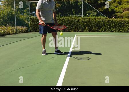 Uomo caucasico anziano che gioca a tennis sul campo con racchetta da tennis Foto Stock