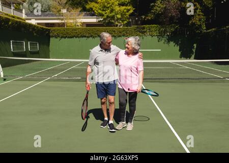 Coppia caucasica senior abbracciando e sorridendo sul campo da tennis Foto Stock