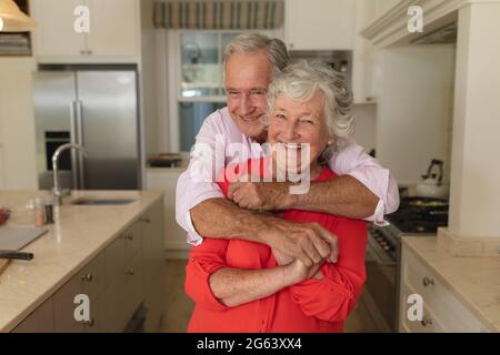 Ritratto di coppia caucasica senior guardando la macchina fotografica e sorridendo in cucina Foto Stock