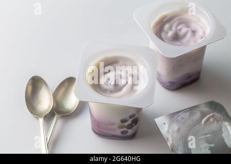 Tazze di yogurt alla mirtillo blu con yogurt naturale e bacche blu - due tazze e due cucchiai con yogurt alla frutta cremosa isolato su sfondo bianco con copia Foto Stock