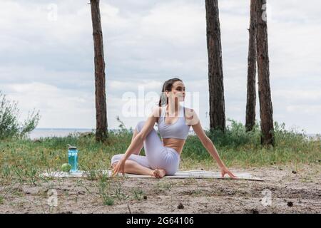 giovane sorridente seduto che pratica yoga sul tappetino nella foresta Foto Stock