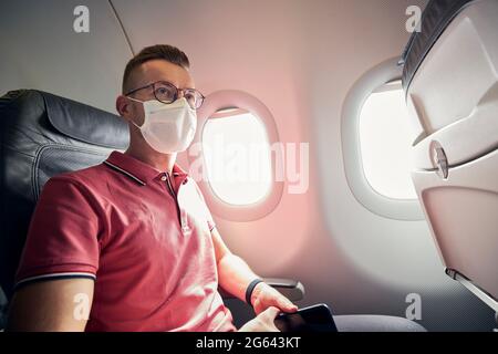 Ritratto del passeggero con maschera protettiva in aereo. Temi che viaggiano in una nuova protezione normale e personale durante la pandemia covid-19. Foto Stock