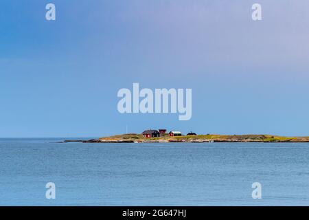 Varberg, Svezia - 20 giugno 2021: Piccole case rosse su un istmo di terra nel mezzo di un oceano calmo sotto un cielo blu Foto Stock