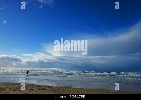 Lone surfer che entra in acqua alla spiaggia di Perranporth, Cornovaglia, Regno Unito - John Gollop Foto Stock