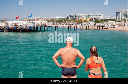 Antalya, Turchia-29 giugno 2021: Padre e figlia si preparano a saltare in mare dal molo d'estate ad Antalya. Abbronzatura offuscata di persone e hotel Foto Stock