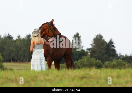 Ritratto di una bella giovane allegra donna con cappello da cowboy e cavallo all'aperto. Prato nel giorno d'estate Foto Stock