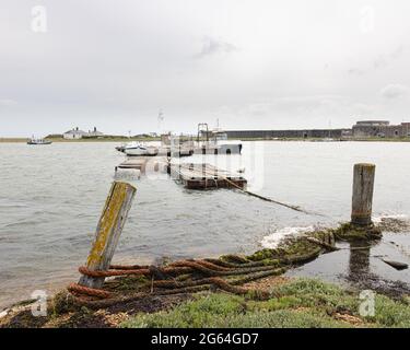 Hurst Point, Hampshire, Regno Unito, 22 giugno 2021: Piccole barche ormeggiate presso un molo di rossackle. L'Hurst Ferry si avvicina al faro mentre si dirige verso il castello di Hurst. Foto Stock