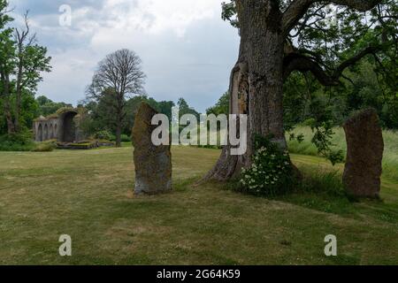 Alvastra, Svezia - 20 giugno 2021: Grandi massi obelischi con le rovine dell'abbazia di Alvastra sullo sfondo Foto Stock