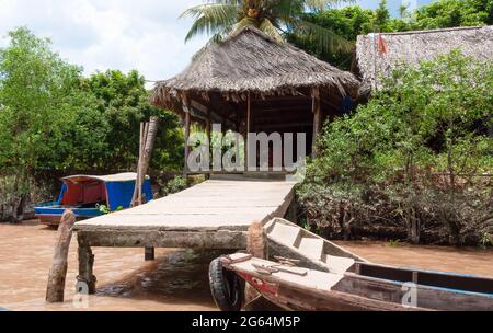 Molo e casa di paglia sul delta del Mekong in Vietnam con una barca di pesca in legno ancorata. Foto Stock