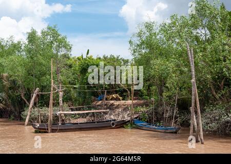 Imbarcazione da pesca in legno attraccata sul delta del Mekong in Vietnam circondata da alberi verdi. Foto Stock