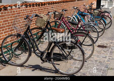 Koge, Danimarca - 12 giugno, 2021 file di molte biciclette colorate parcheggiate contro un muro di mattoni rossi Foto Stock