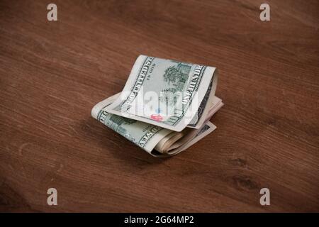 Pila di soldi delle fatture del dollaro degli Stati Uniti piegata a metà su sfondo di legno. Banconota da cento dollari danneggiata dai francobolli d'inchiostro Foto Stock