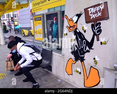 Gli uomini siedono accanto a un'immagine del personaggio dei cartoni animati di Daffy Duck, parte di un percorso artistico Looney Tunes che ha aperto a Manchester, in Inghilterra. Foto Stock