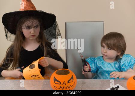 Due sorelle ragazze in costumi di una strega e bianco neve seduta ad un tavolo ritagliato decorazioni di carta per la festa di Halloween Foto Stock
