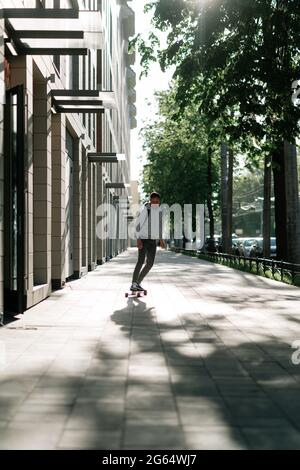 Giovane uomo casual a bordo di una tavola da surf per lavorare o studiare lungo la strada della città. Concetto di stile di vita giovanile Foto Stock