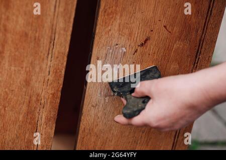 primo piano la mano di una donna tiene una spatola e mette stucco su un buco in un vecchio tavolo di legno, riciclando laboratorio Foto Stock