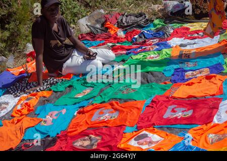 Venditore di strada che vende la varietà di t-shirt stampate su uno stand di terra Foto Stock