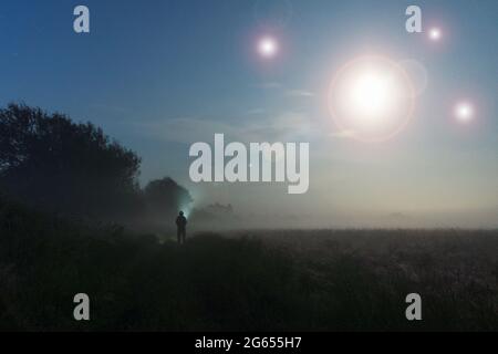 Un concetto di fantascienza moody, di una figura in piedi in un campo con luci UFO che illuminano nel cielo. In una notte sciocchiata. Foto Stock