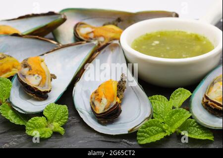 Le cozze con salsa piccante sono poste su uno sfondo di pietra nera. Foto Stock