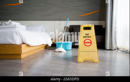 Un cartello giallo 'NO ENTRY' posto al piano della camera d'albergo. Durante la pulizia. Un mop e un secchio d'acqua sullo sfondo Foto Stock