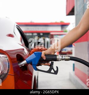 La mano del lavoratore della stazione di benzina che tiene la pompa blu del gas del benzene, riempiendo il serbatoio rosso dell'automobile di sport. Primo piano Foto Stock