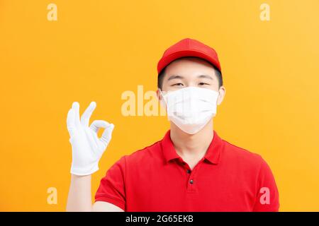 Uomo di consegna o corriere in maschera e guanti che mostrano OK, segno OK Foto Stock