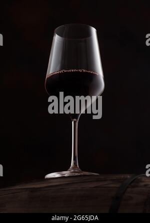 Bicchiere di cristallo di vino rosso sulla parte superiore del barile di legno su sfondo nero. Foto Stock