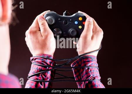 filo del joystick avvolto intorno alle mani delle persone, concetto di dipendenza dai videogiochi Foto Stock