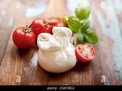 Burrata su tavola di legno d'annata. Formaggio morbido con pomodori e foglie di basilico su tavola di legno. Gustosa burrata con mezzo pomodoro. Foto Stock