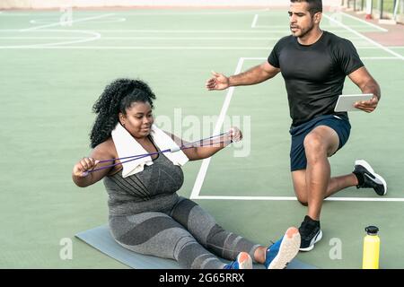 Personal trainer che lavora con una donna curvy spiegandole gli esercizi Routine - concetto di stile di vita delle persone sportive Foto Stock