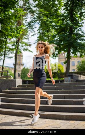 Una giovane bella donna bionda con un fisico sportivo in una T-shirt nera e in shorts nero stretto sport corre le scale Foto Stock