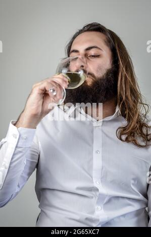 ritratto di un giovane uomo d'affari medio orientale con barba e capelli lunghi bevendo un bicchiere di vino bianco fresco Foto Stock