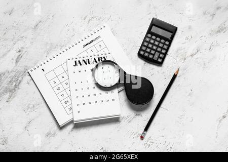 Capovolgi calendari, matita, calcolatrice e lente di ingrandimento su sfondo chiaro Foto Stock