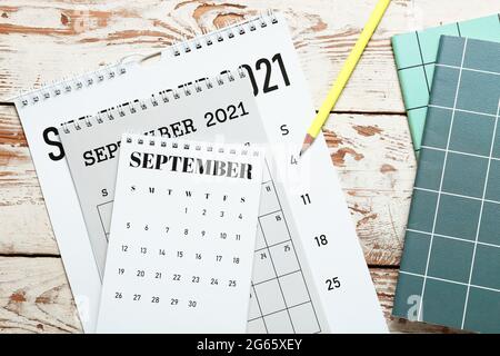 Capovolgi calendari, quaderni e matita su sfondo di legno chiaro Foto Stock