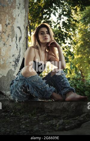 tramp ragazza in jeans strappati si siede in vecchie rovine sporche Foto Stock