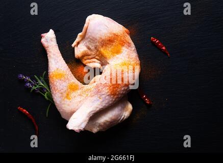 Concetto di cibo quarti di pollo crudo con spezie su tavola di pietra ardesia nera con spazio di copia Foto Stock