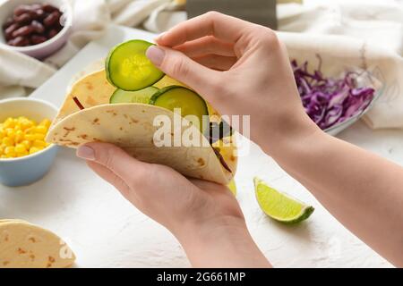 Donna che fa taco gustoso su sfondo chiaro, primo piano Foto Stock