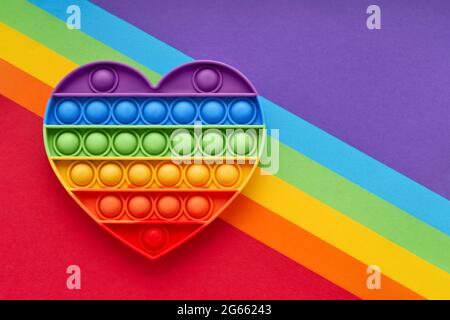 Colorato trendy Pop IT cuore forma fidgets giocattolo per bambini su uno sfondo arcobaleno. Giocattolo anti-stress, sviluppo delle capacità motorie di mani e dita Foto Stock