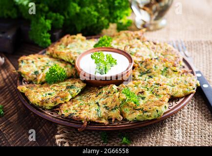 Frittelle di zucchine. Frittelle vegetariane di zucchine con salsa su fondo di legno. Cibo sano. Foto Stock