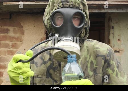 Un uomo in una maschera a gas beve acqua dalla conduttura del tubo. Apocalypse sete di acqua in ambiente di inquinamento salvare il concetto di inquinamento idrico. Foto Stock