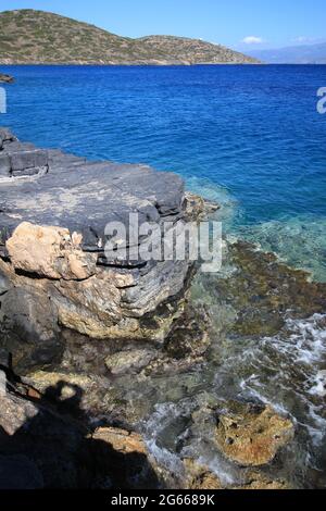 Isola Spinalonga, costiero vicino Elounda, Creta, Grecia. Rocce vulcaniche nere Foto Stock