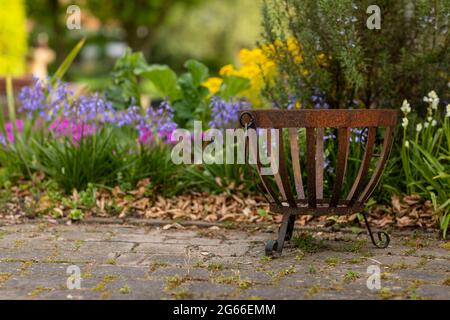 Arrugginito vecchio pozzo del fuoco di metallo che si trova in un bellissimo giardino idilliaco con fiori, alberi e vegetazione in una giornata di sole che crea un paesaggio attento Foto Stock