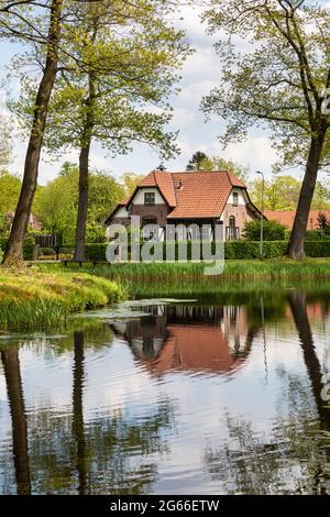 Tipico olandese autentica vecchia casa vicino al fiume con riflessi in acqua, circondato da alberi e vegetazione creando un paesaggio attento su un sole Foto Stock