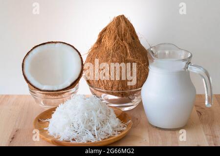 Prodotti di cocco, un intero cocco, mezzi, latte grattugiato e di cocco su tavolo di legno, sfondo bianco e spazio copia. Foto Stock