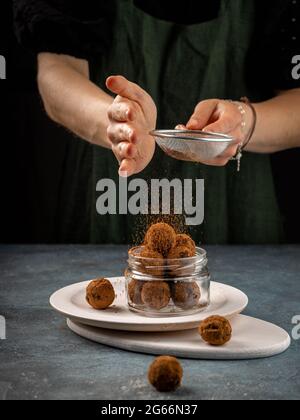 Una donna cospargete le palle di cioccolato con polvere di cacao. Concetto di cucina sana Foto Stock