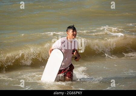 Uribia, la Guajira, Colombia - Maggio 27 2021: Giovane uomo Latino bagnato sta portando una Surfboard dopo aver scivolato sulle dune di Taroa e cadendo nel Mare W. Foto Stock